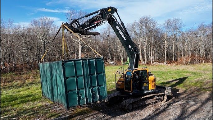 Bagger hebt einen großen grünen Schiffscontainer mit Gurten an.